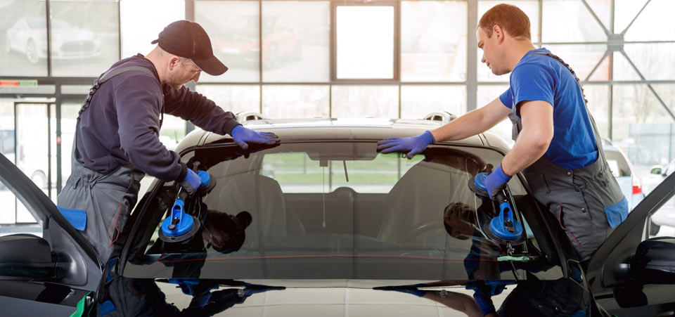 Dealership technicians installing a new car windshield with assistance from GMS software